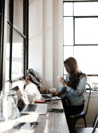 Frau trinkt Kaffee auf der Arbeit vor dem Laptop
